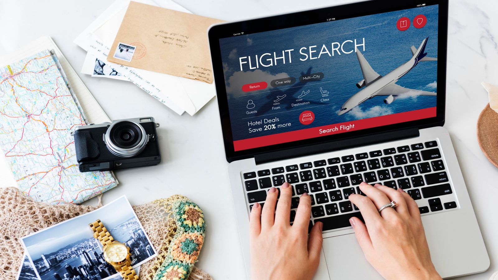 A traveller searching for flights on a laptop, surrounded by a map, camera and travel photos